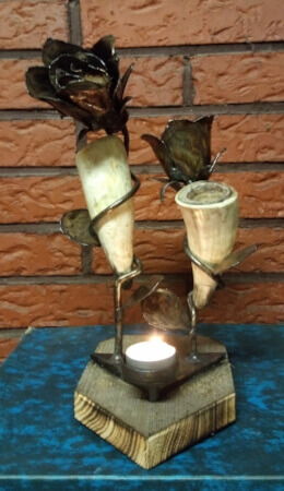 Puunpäälle tehty kynttilänjalka, jossa on kaksi ruusua pitämässä lehmänsarvia